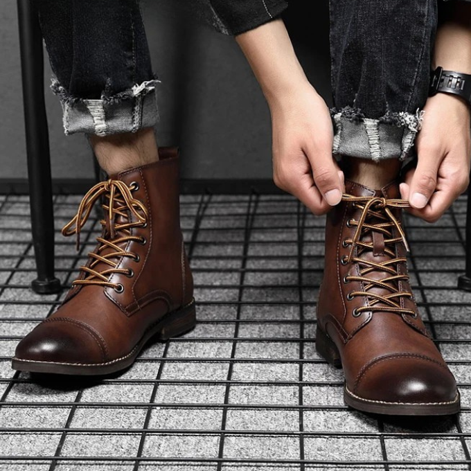 Man tying laces on brown leather ankle boots with jeans