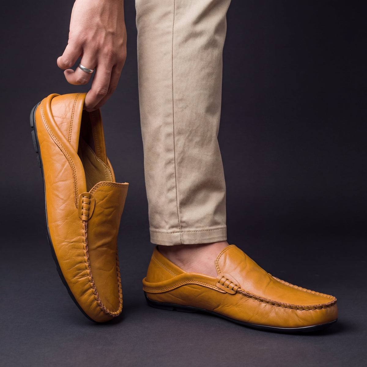 Man holding mustard leather moccasin while wearing matching pair with chinos